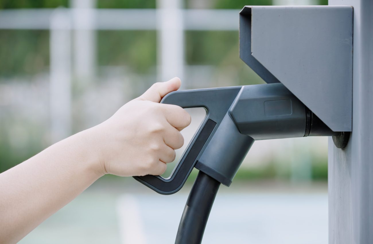 Closeup hand holding electric car charger head plug for charging battery EV car at ev charger station box